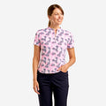 A woman modeling a short-sleeve collared polo-style top with a pink base and an allover abstract print in dark blue and white, paired with dark navy pants against a light gray studio background.