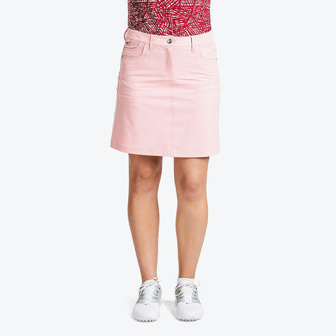 A woman wearing a pink skort and white sneakers, standing against a white background.